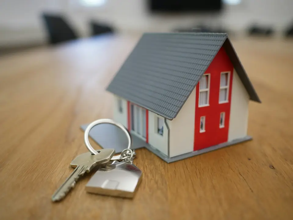 Een houten huismodel met een sleutel op een houten tafel