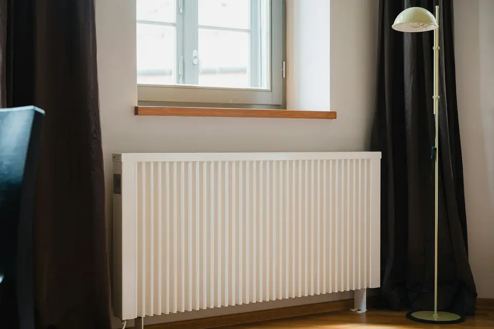 Witte radiator onder een raam in een lichte kamer met donkere gordijnen