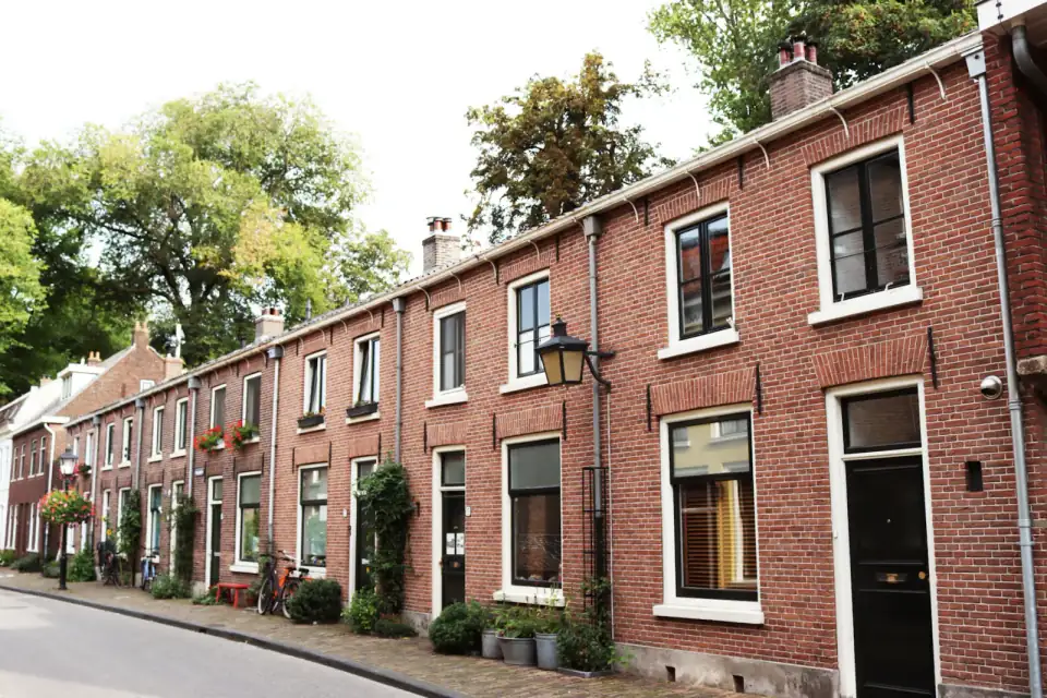 Een rij bakstenen rijtjeshuizen met witte kozijnen en voortuintjes