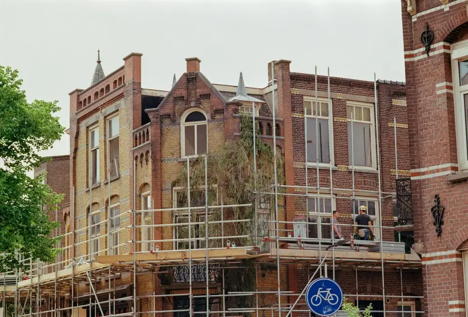 Bakstenen herenhuizen in een Nederlandse straat met een steiger langs de gevel en twee bouwvakkers op de steiger