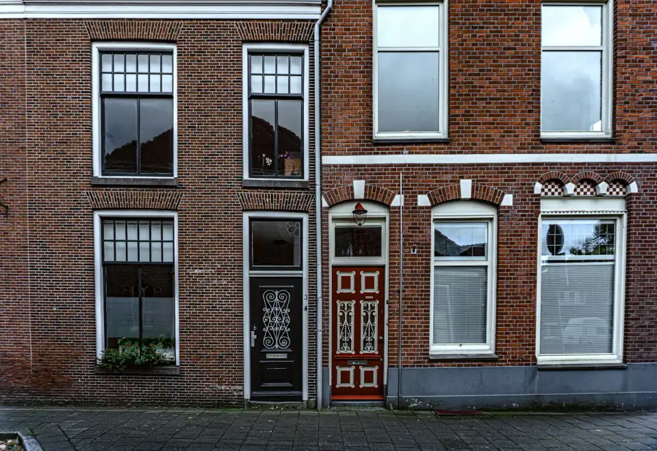 Oude bakstenen herenhuizen in een Nederlandse straat, met een rode voordeur en witte kozijnen
