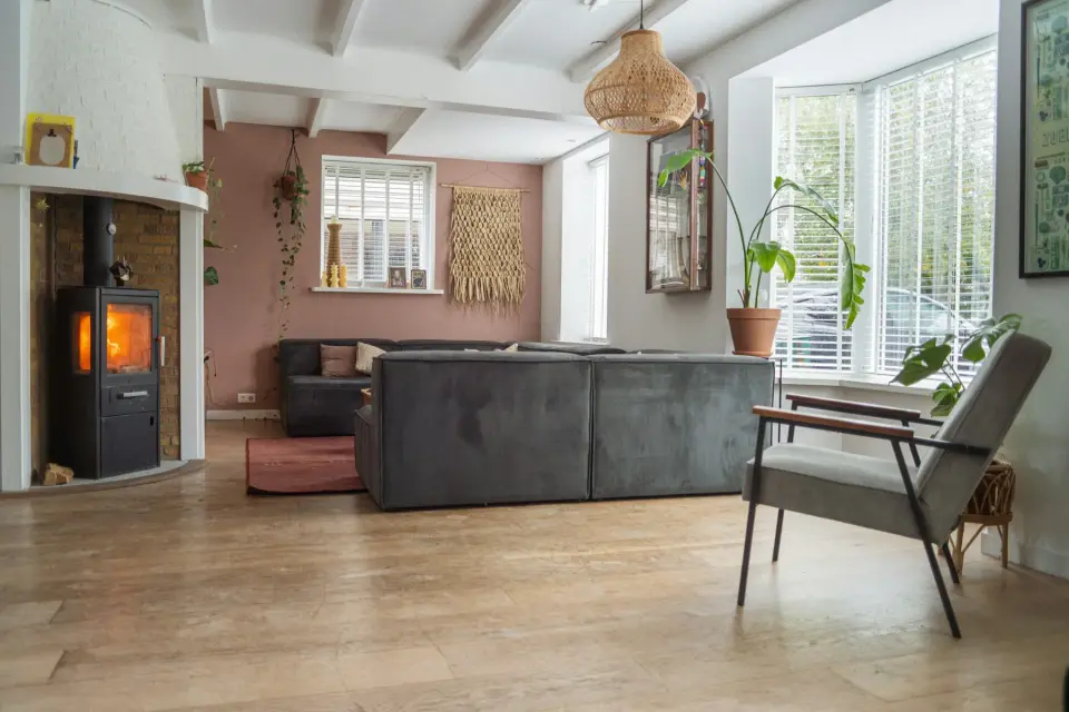 Lichte woonkamer met een houten vloer, een grijze bank en een houtkachel